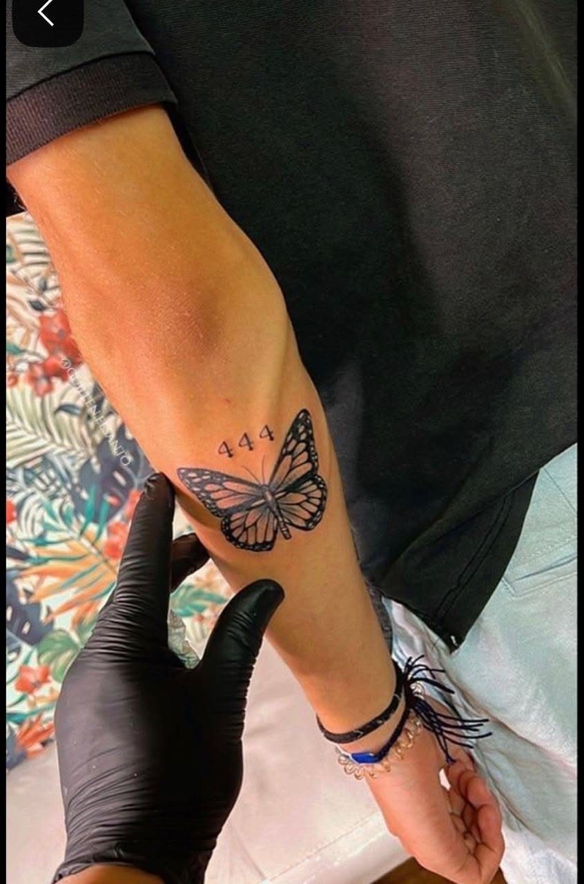 A butterfly tattoo with the numbers 444 on a person's upper forearm.