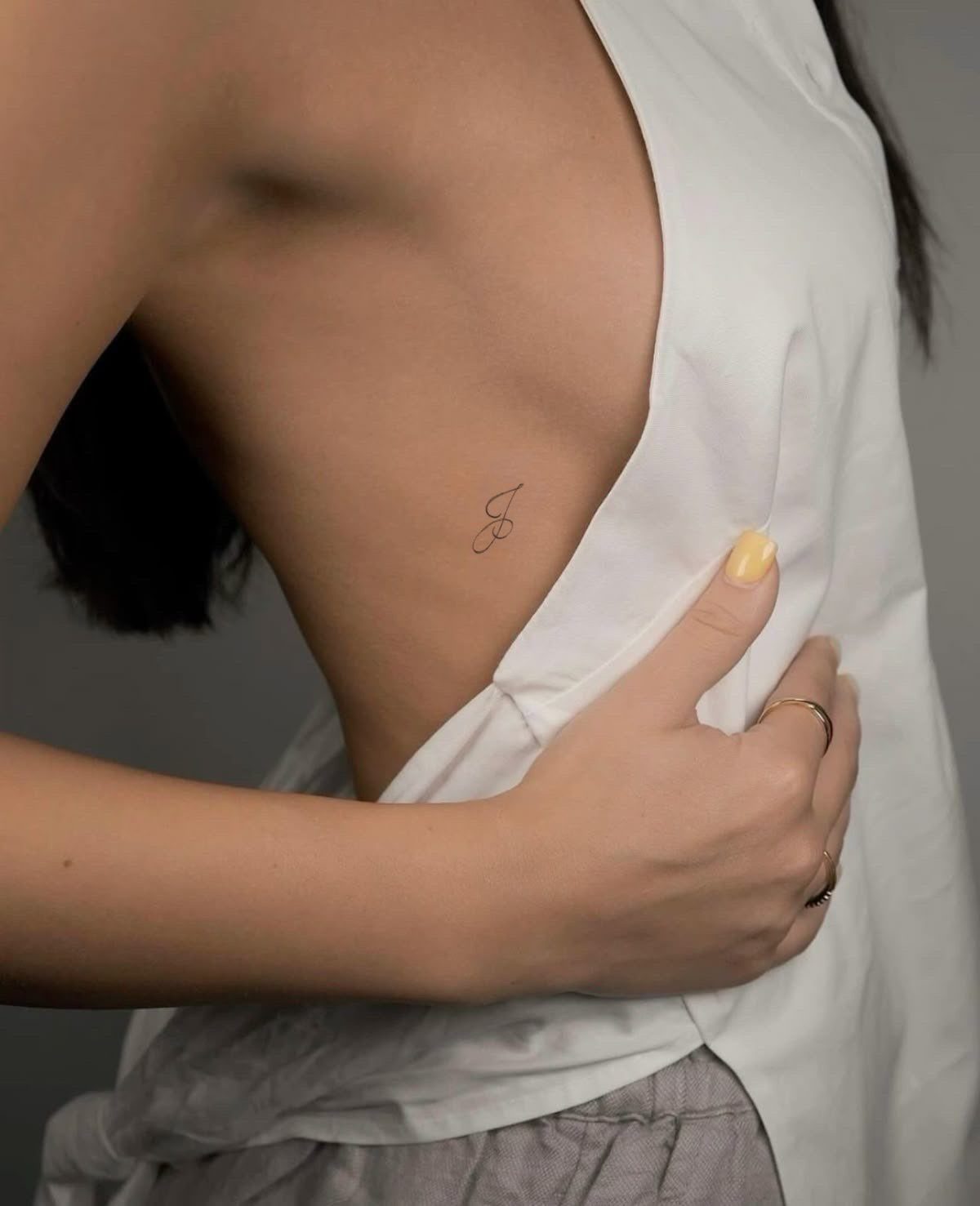 A small cursive letter tattoo located on the side ribs of a person.