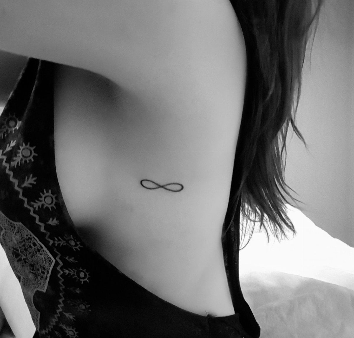 A small black infinity symbol tattoo located on a person's side ribs.