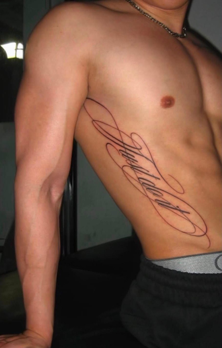 A man's side ribs featuring a large vertical cursive script tattoo with flowing lines.