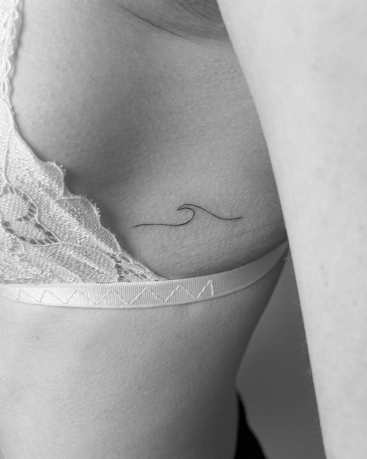 A minimalist fine line wave silhouette tattoo on a person's side ribs.