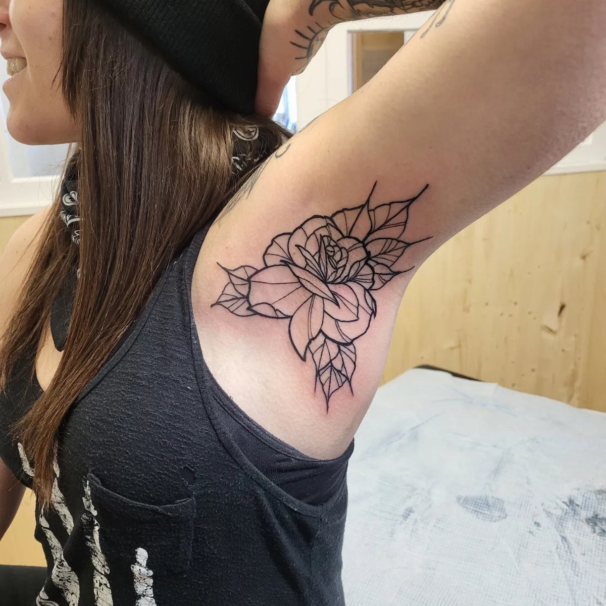 A black line art rose tattoo placed on a person's underarm area.