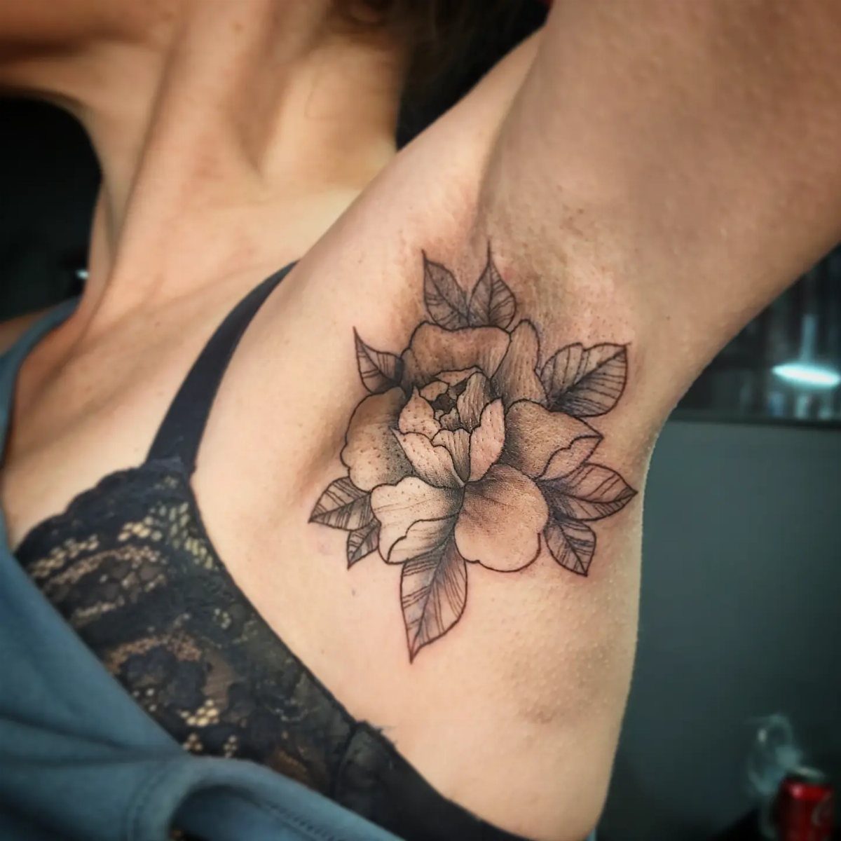 A black and grey peony floral tattoo placed on a person's underarm skin.