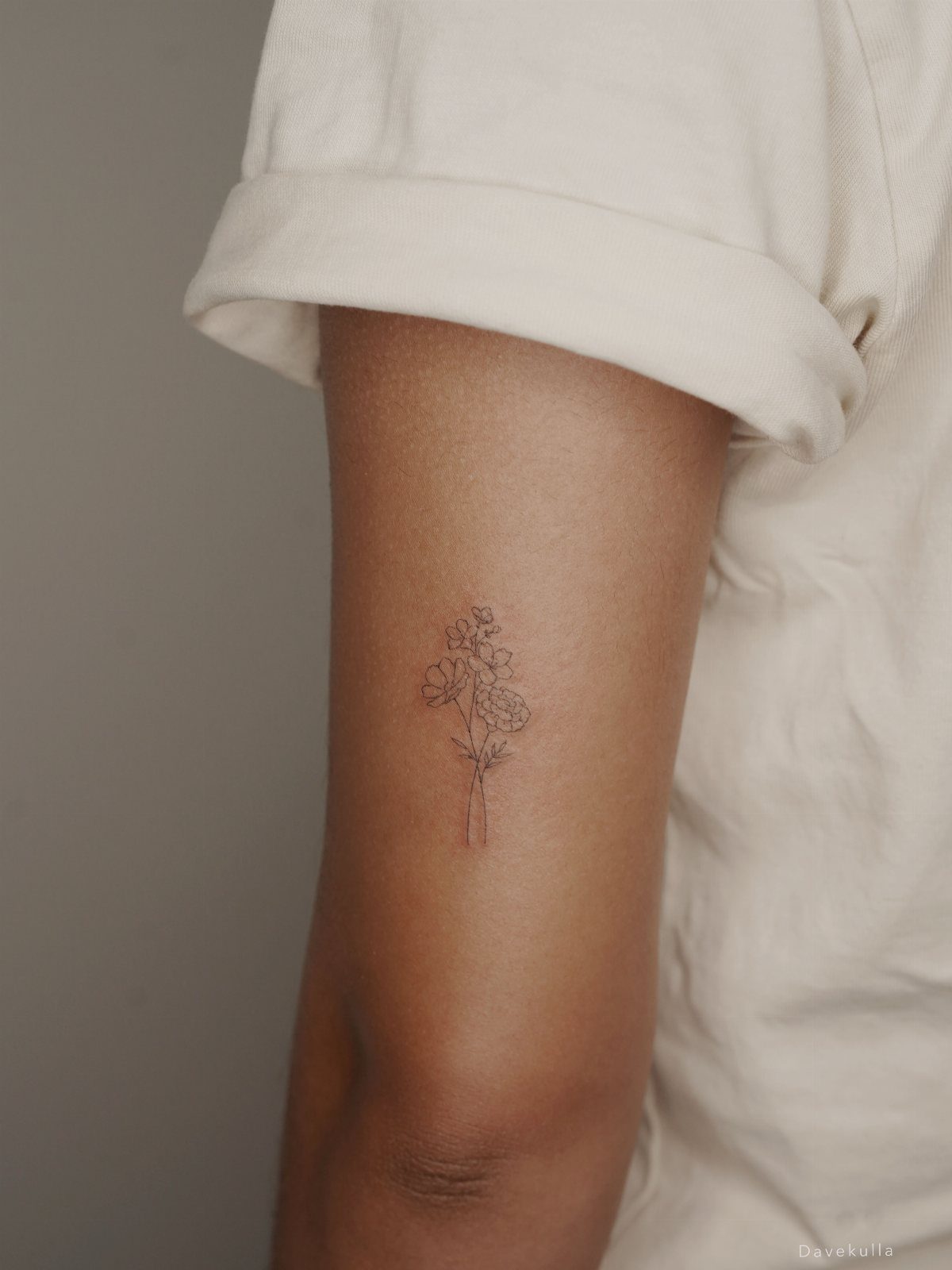 A delicate black ink fine line flower bouquet tattoo on a person's upper arm.