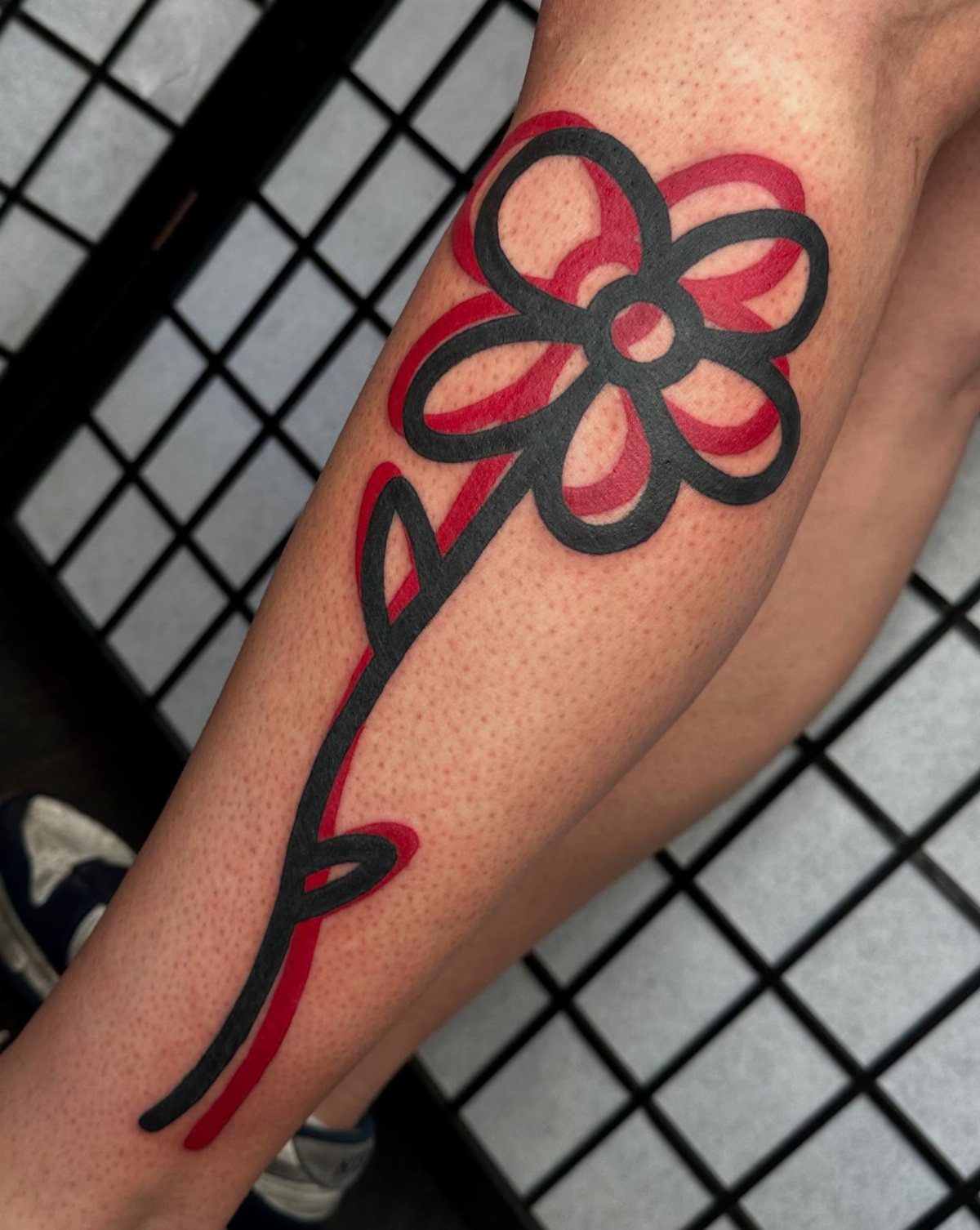 A simple black and red hand-drawn style flower tattoo on a person's leg.