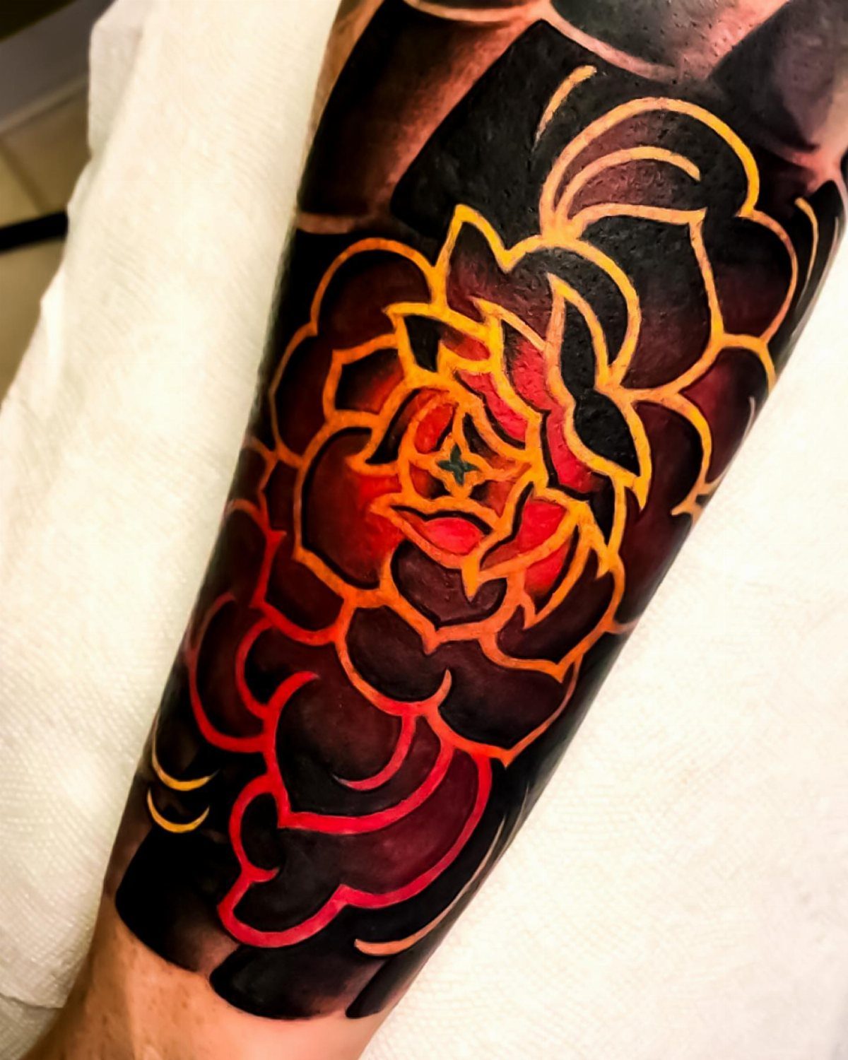 A large colorful floral tattoo with bold black outlines and red and orange shading on an arm.