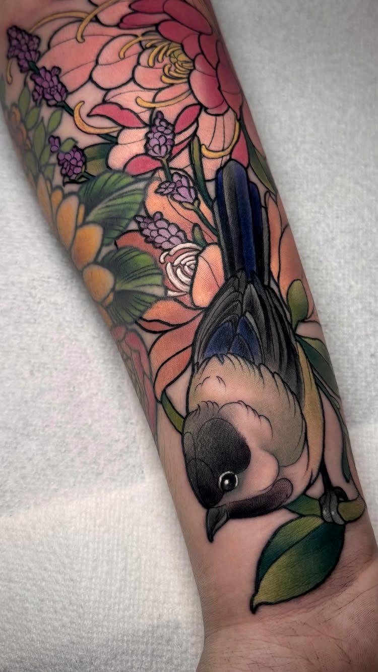 A colorful tattoo of a bird surrounded by large pink and orange peony flowers on an arm.
