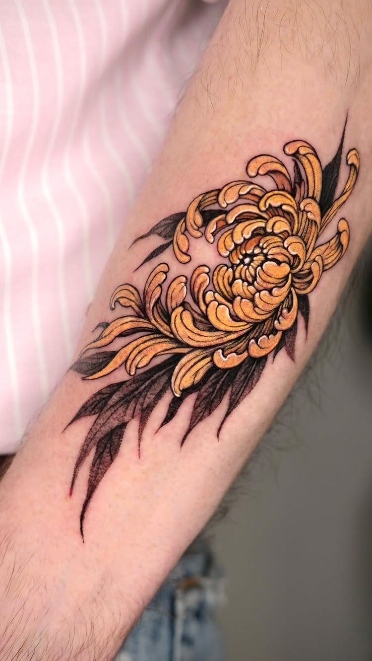 A large orange chrysanthemum tattoo with dark leaves on a person's forearm.