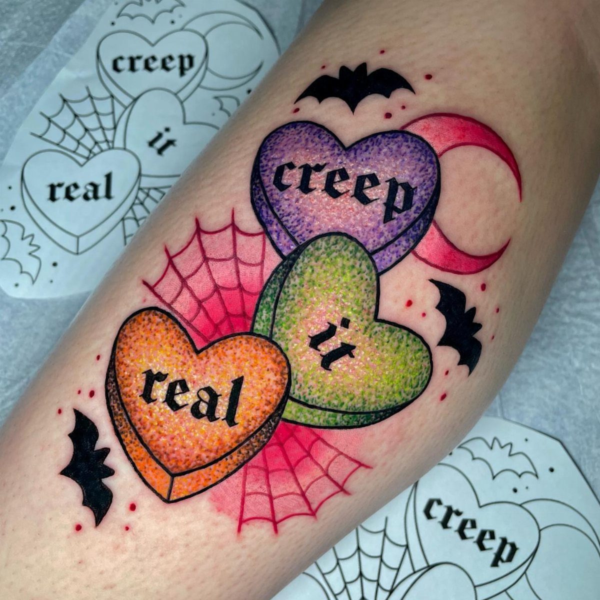 Heart-shaped candy tattoos on an arm with bats, a moon, and a spiderweb design.