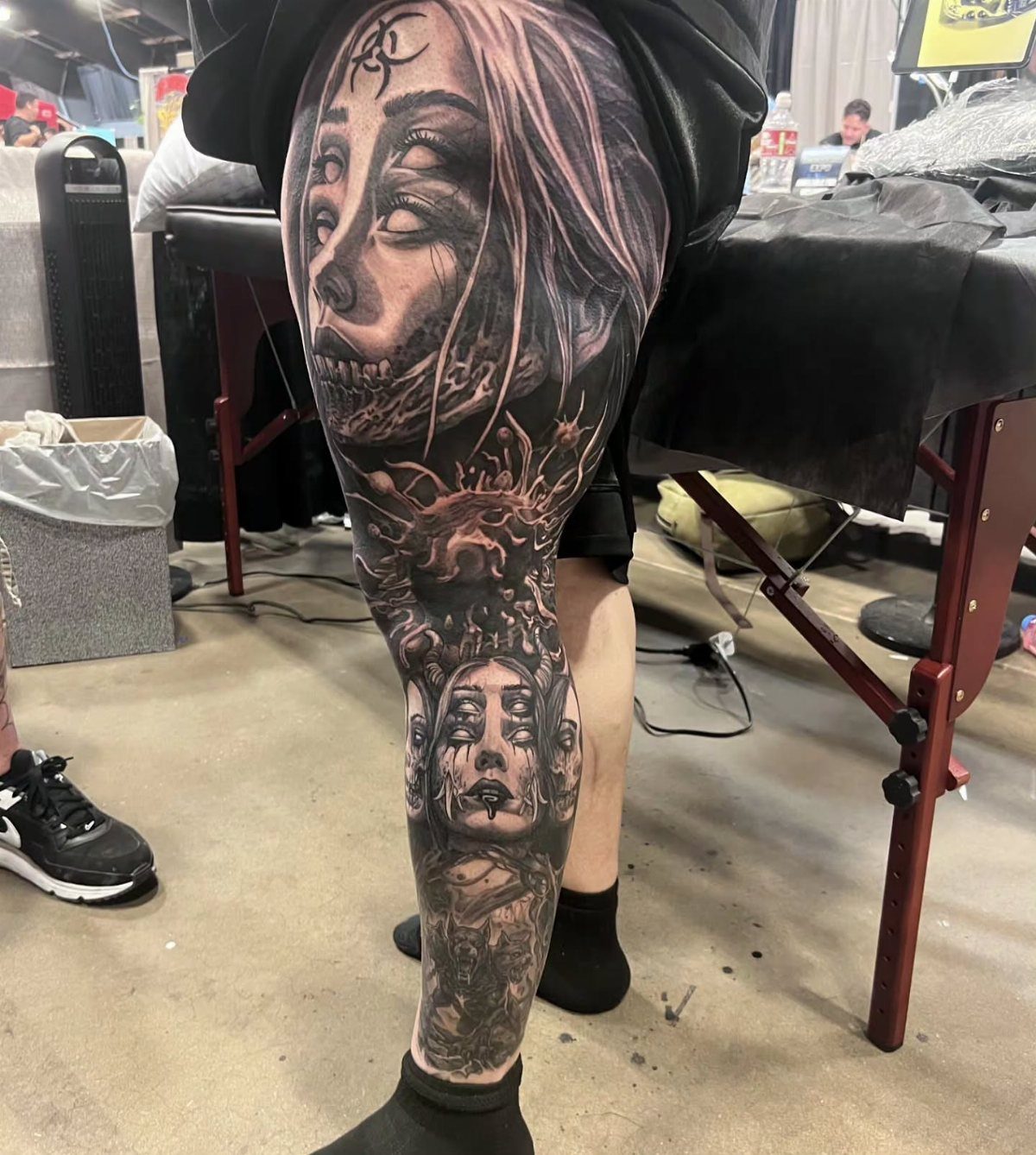 Large black and grey realism tattoo on a person's leg featuring detailed, eerie female faces.
