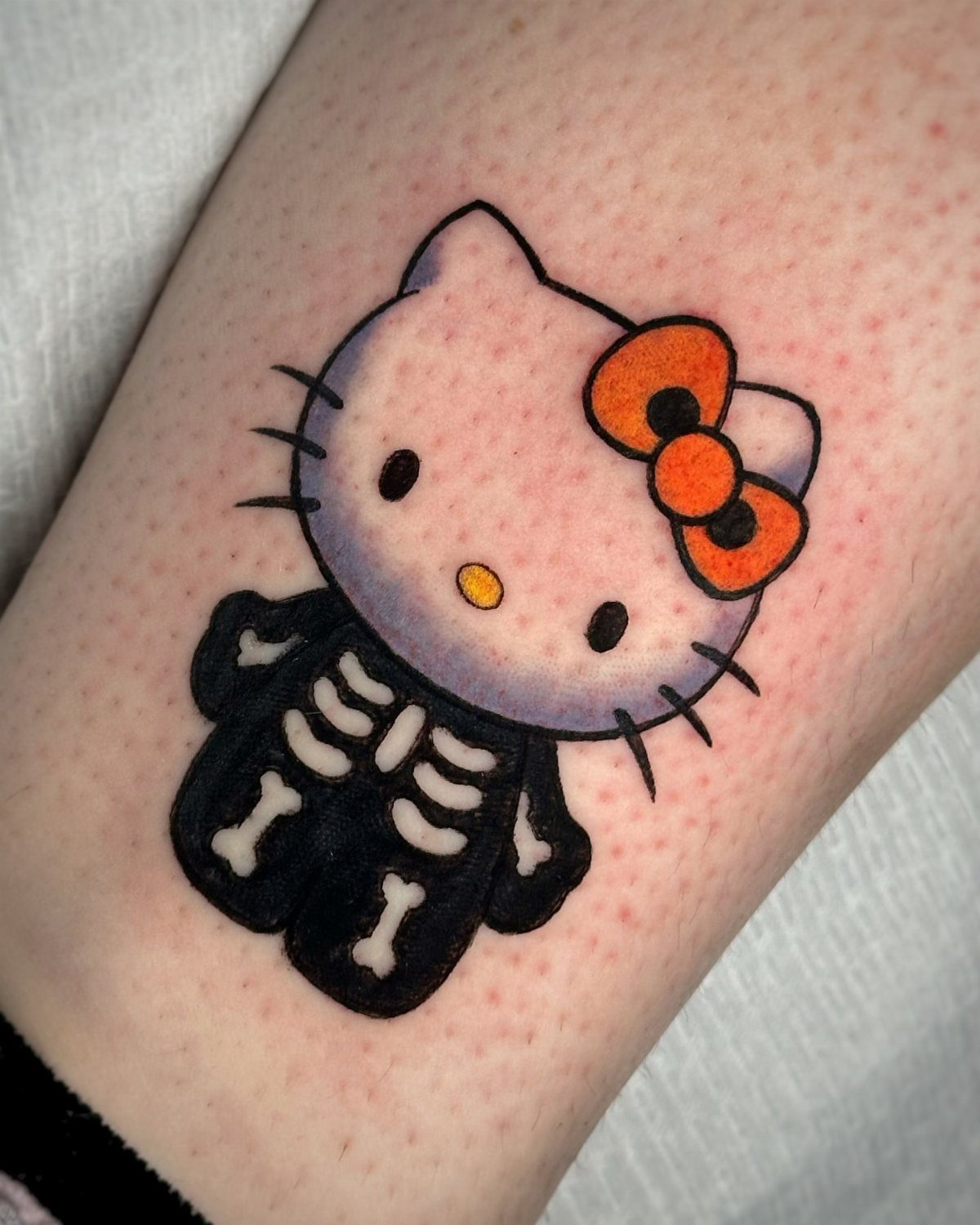 Hello Kitty tattoo wearing a black skeleton suit on a person's skin.