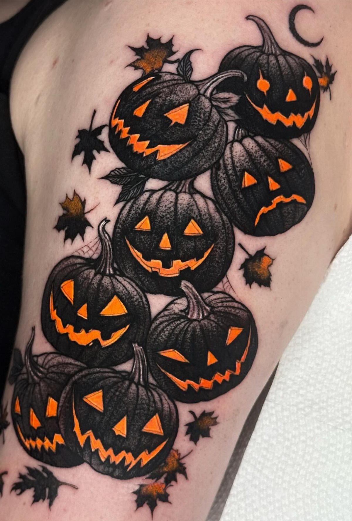 Black and orange jack-o'-lantern pumpkin tattoos with autumn leaves on skin.