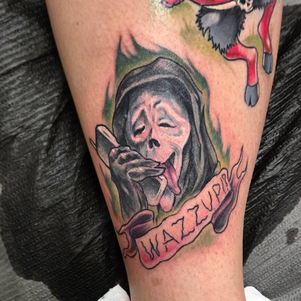Scream Ghostface character tattoo on a leg with a pink banner reading WAZZUP!!!