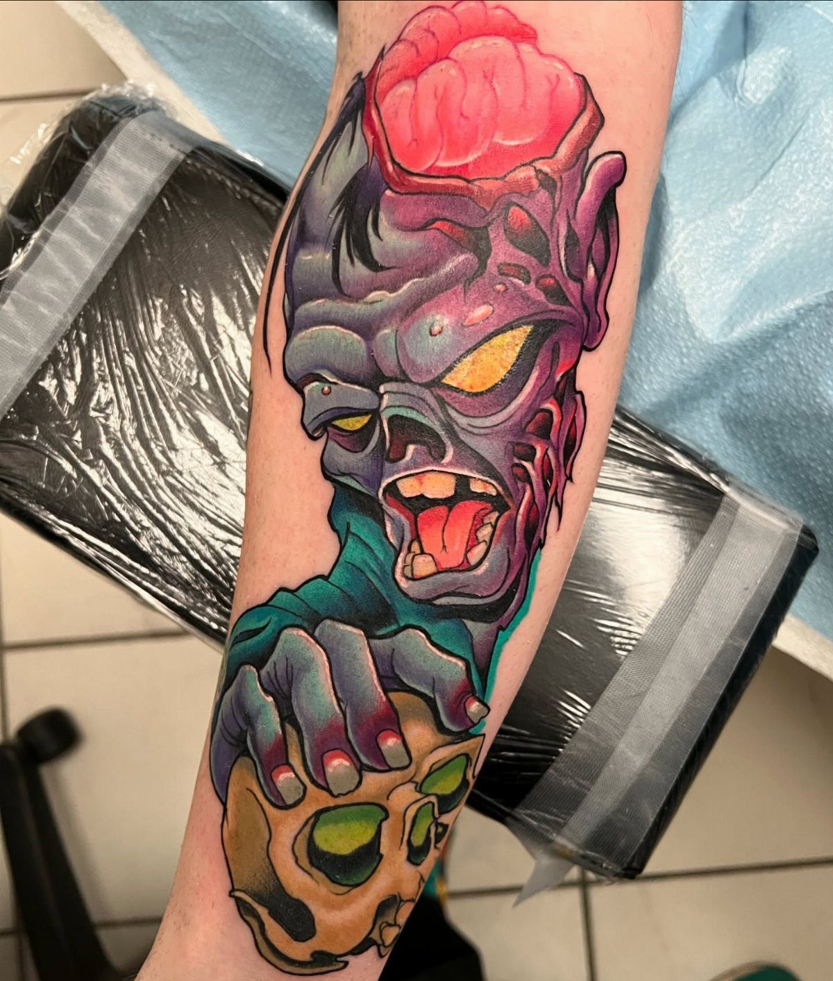 A vibrant zombie tattoo with exposed brain and a skull on a person's forearm.