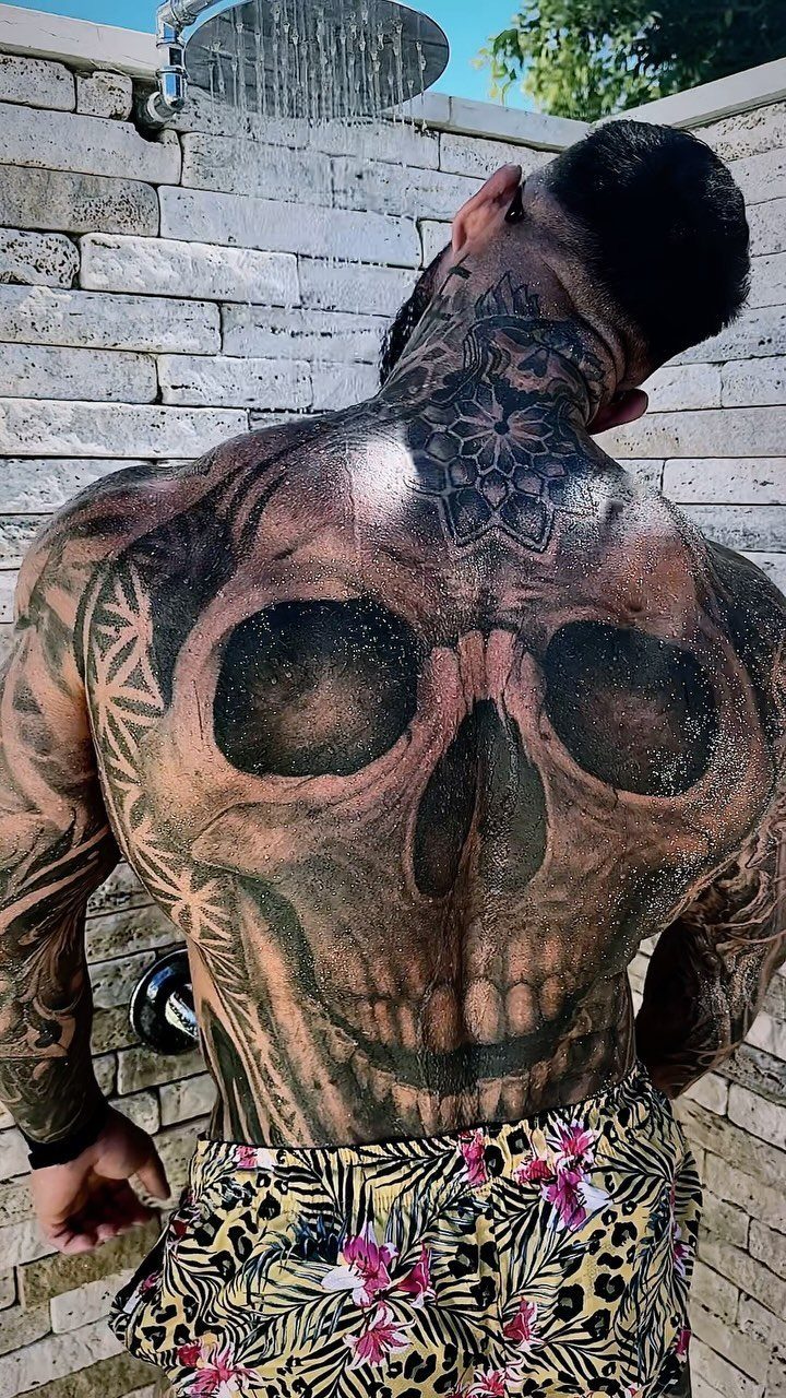 A man with large black ink skull and geometric tattoos covering his entire back.
