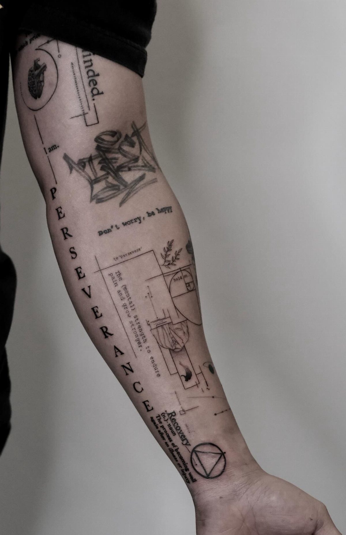 A person's forearm covered in various fine line black ink tattoos and text.