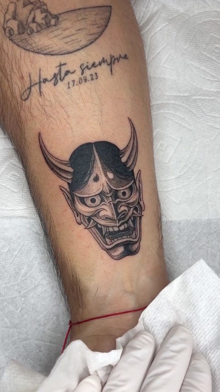 A black and grey Hannya mask tattoo on a person's lower leg skin.