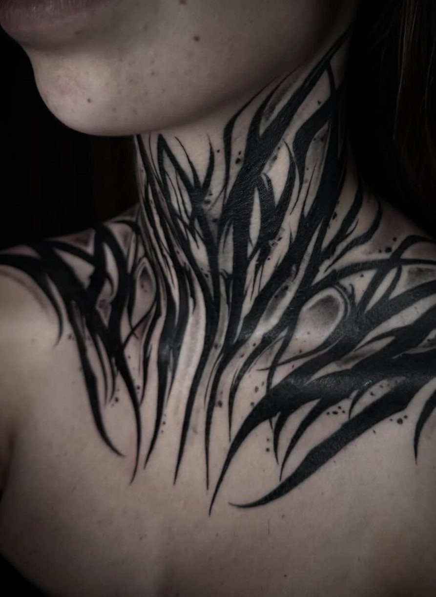 Black tribal style tattoo with sharp flowing lines covering a person's neck and upper chest.