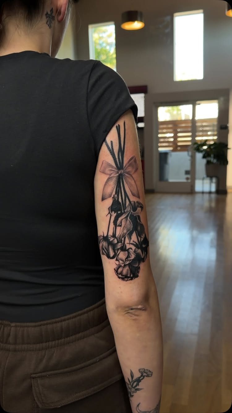 A black ink rose bouquet tattoo with a ribbon on a person's upper arm.