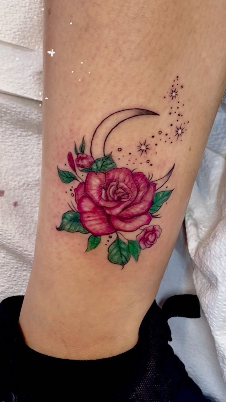 A pink rose tattoo with a crescent moon and stars on a person's leg.