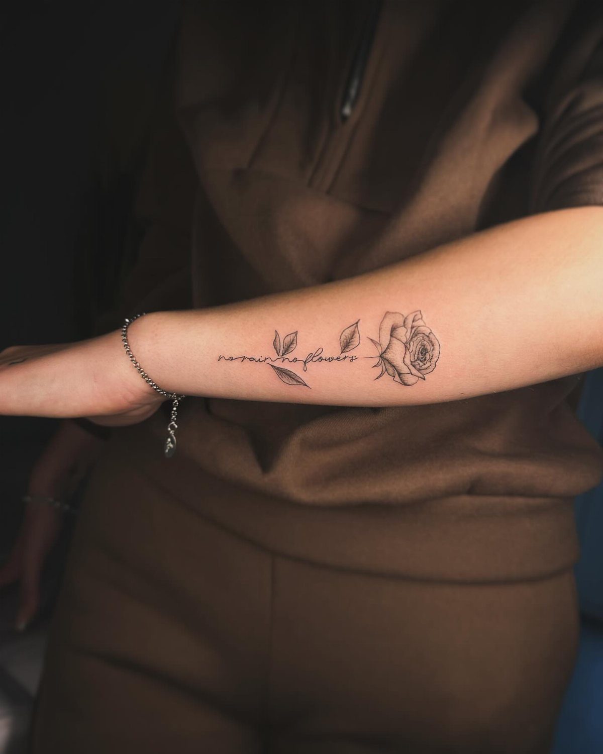 A minimalist black ink rose tattoo with small leaves on a person's forearm.