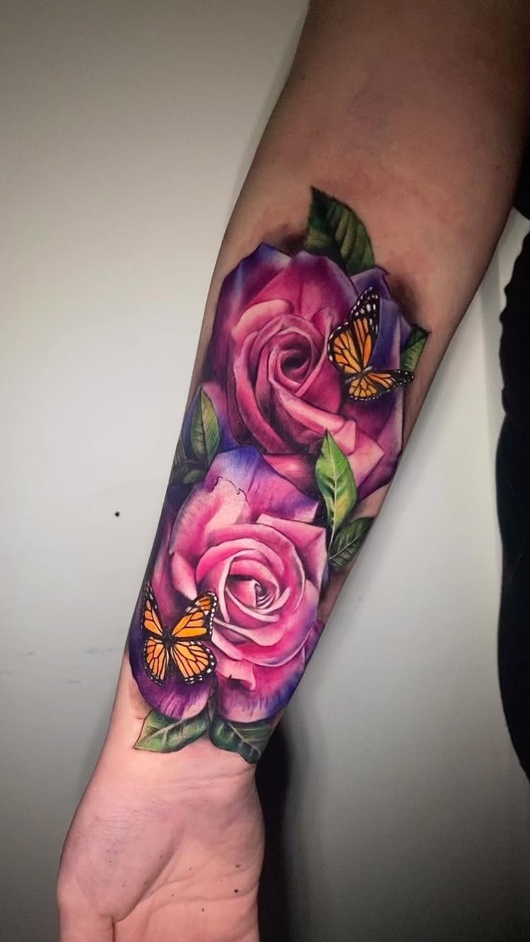 Realistic pink rose tattoos with green leaves and orange butterflies on a person's forearm.