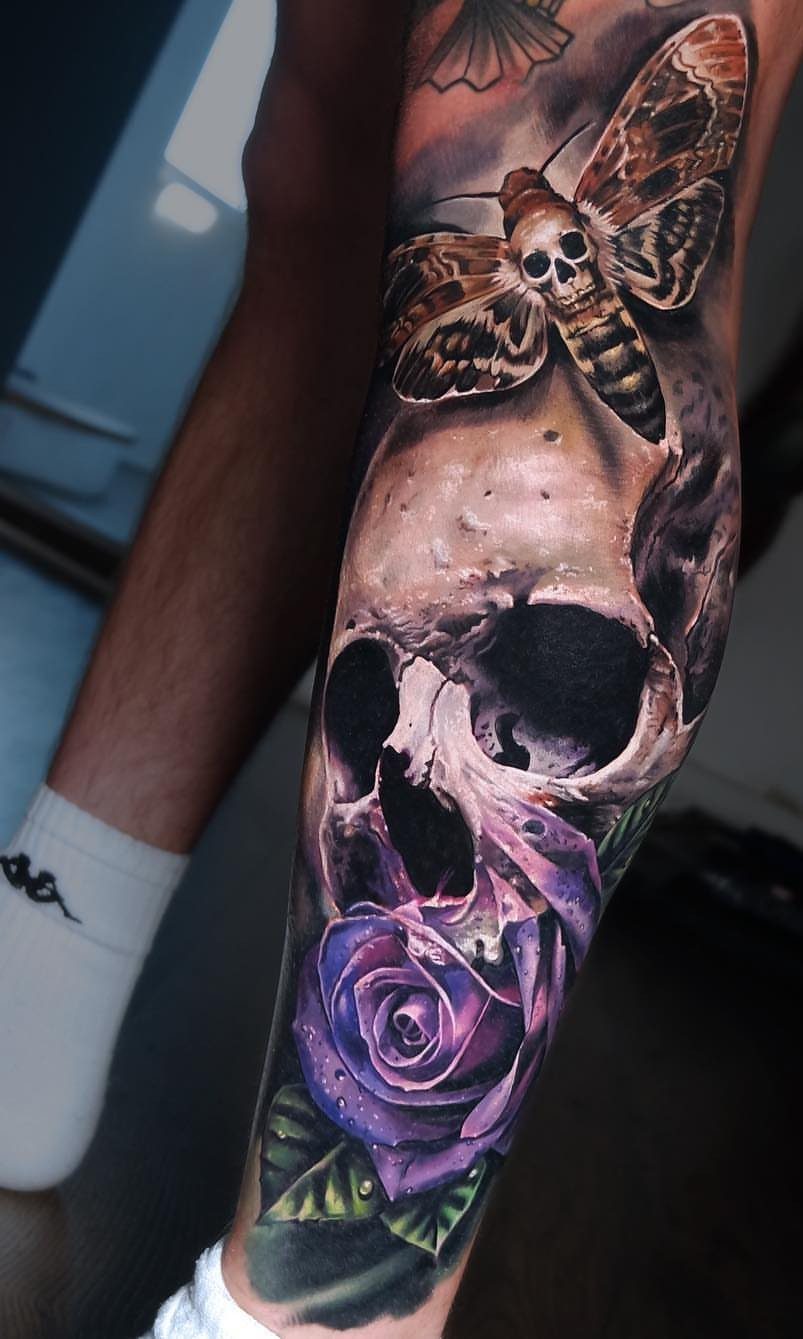 A detailed tattoo on a leg featuring a skull, a purple rose, and a moth.