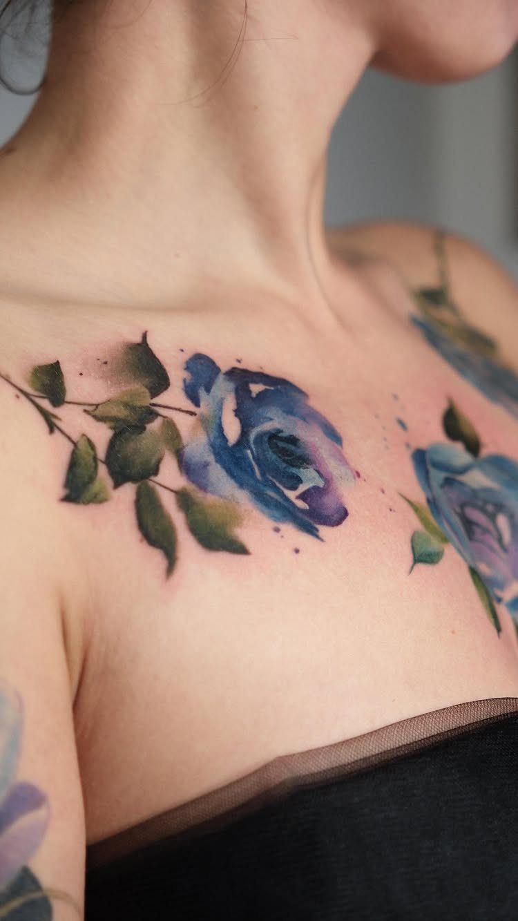Blue and purple watercolor rose tattoos on a person's collarbone and shoulder area.