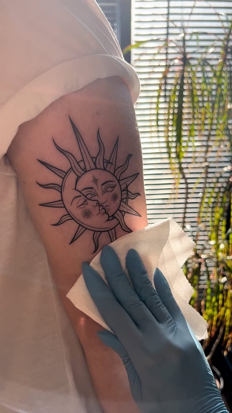 A sun and moon celestial tattoo being cleaned on a person's upper arm.
