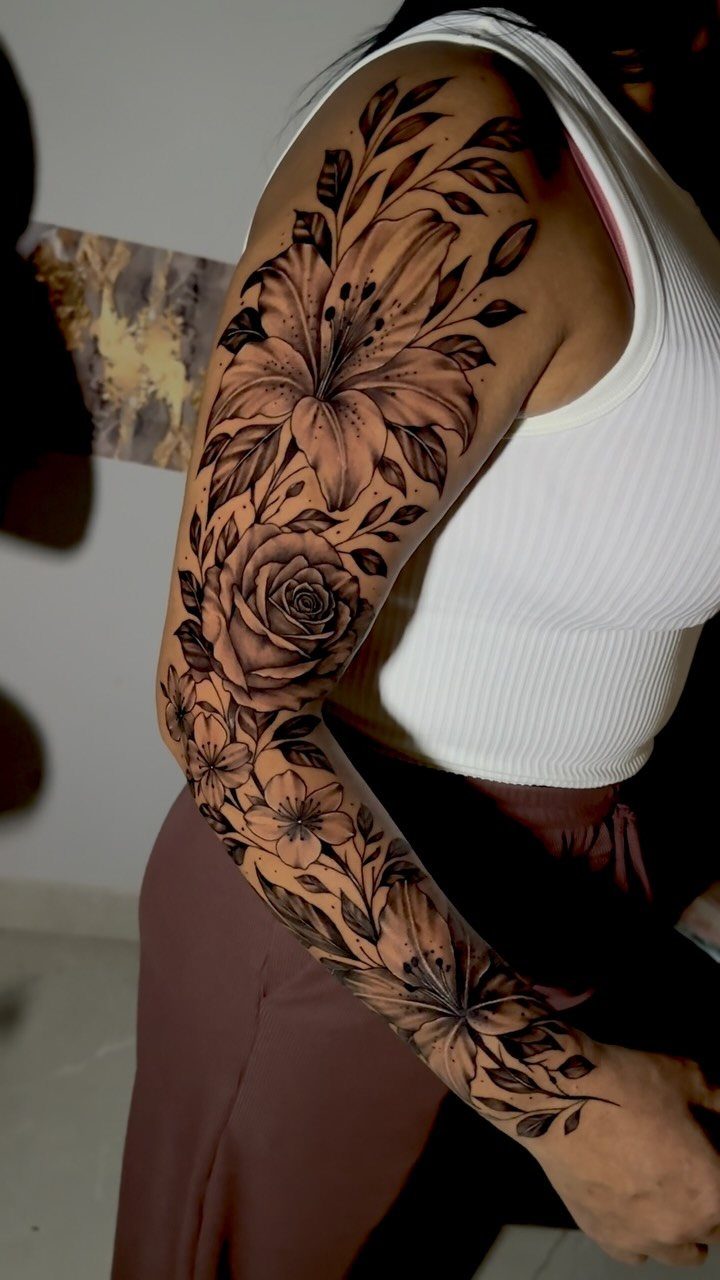 A woman's arm decorated with a large, detailed black and grey floral sleeve tattoo.