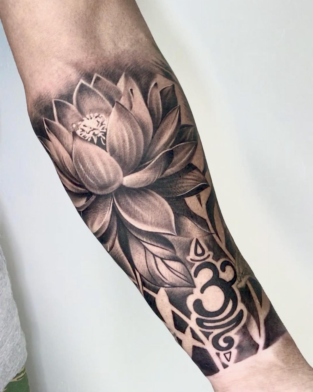 A detailed black and grey lotus flower tattoo with an Om symbol on a person's forearm.