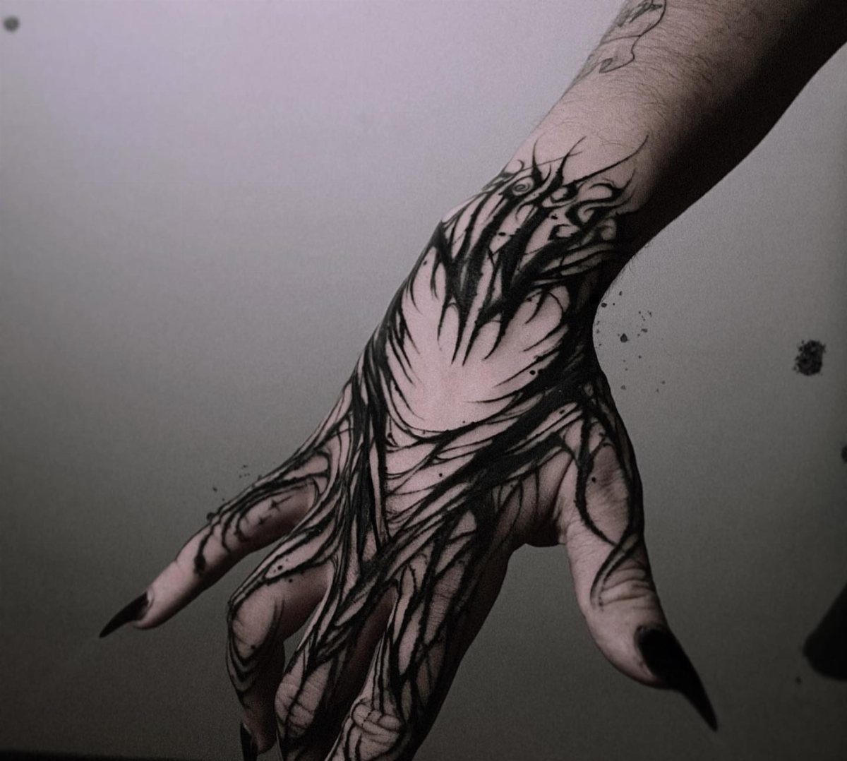 A hand with an intricate black monochrome abstract tattoo covering the back and fingers.