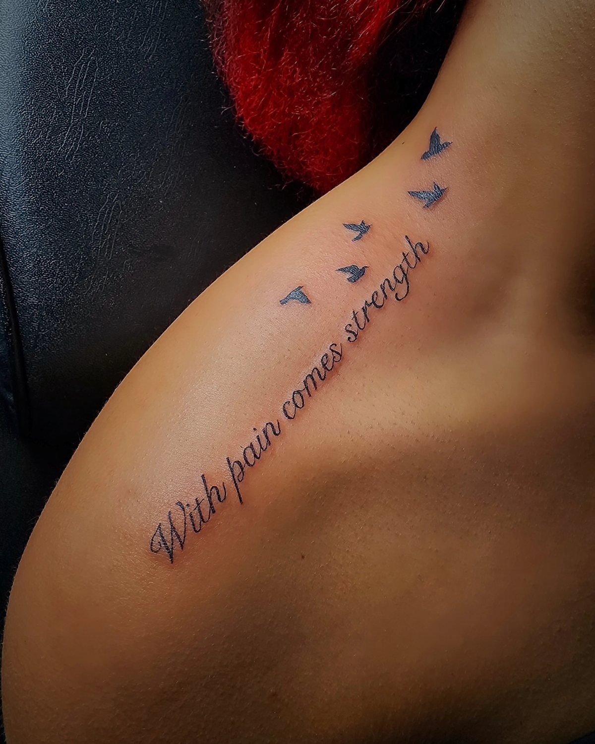 A script tattoo on a person's shoulder reading 'With pain comes strength' with small birds.