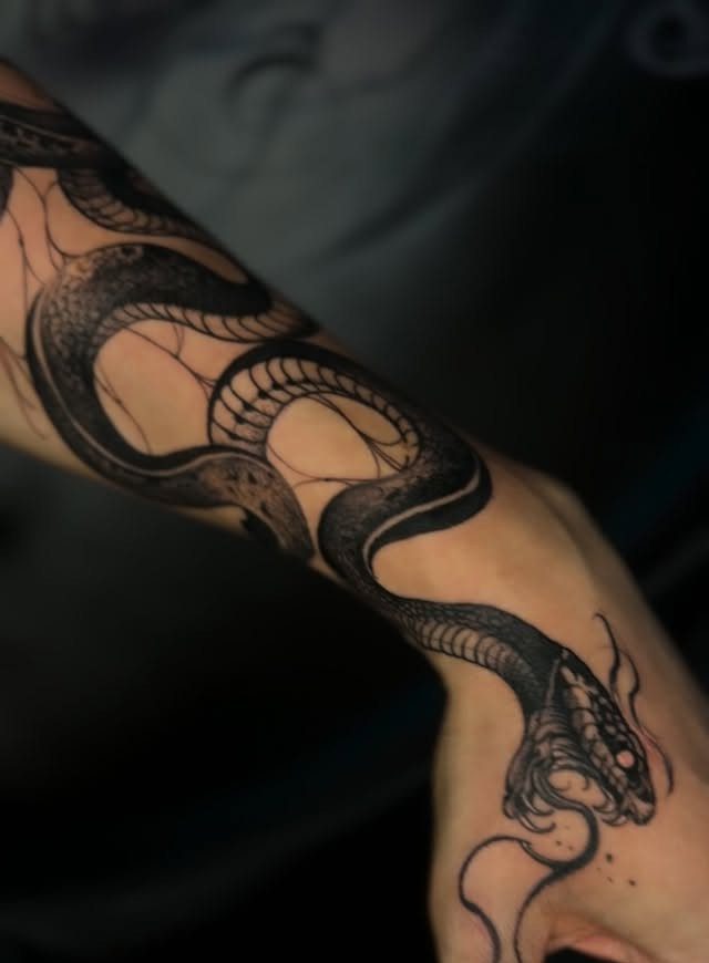 A large black ink snake tattoo winding around a person's forearm and onto their hand.