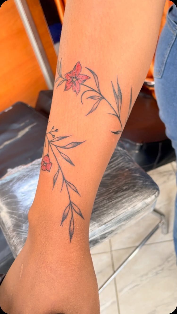 A forearm displaying two delicate vine tattoos with small pink flowers and dark leaves.