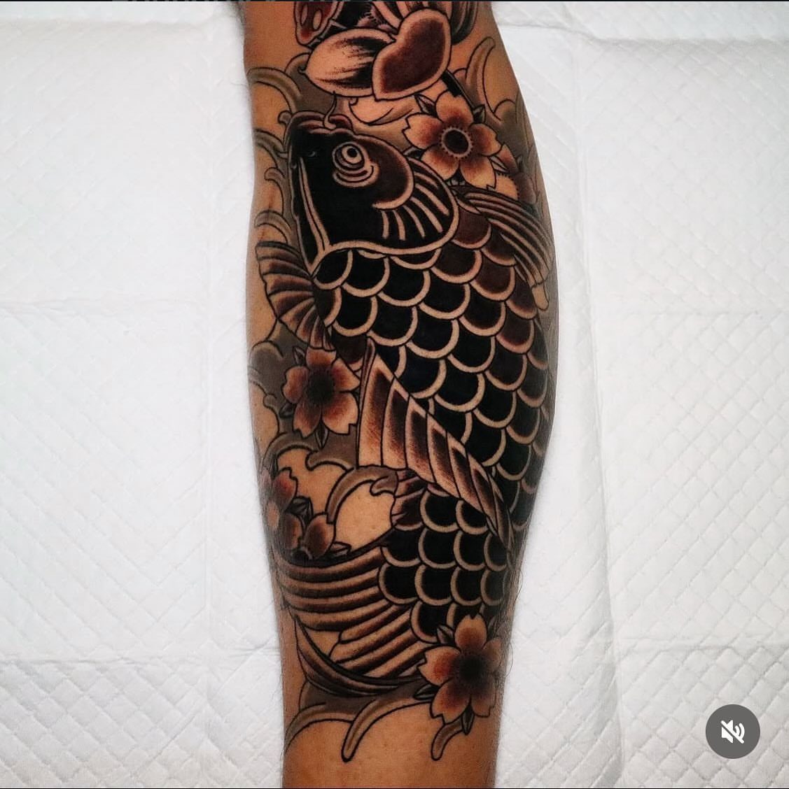 A large koi fish tattoo with cherry blossoms covering a person's leg in black and grey ink.