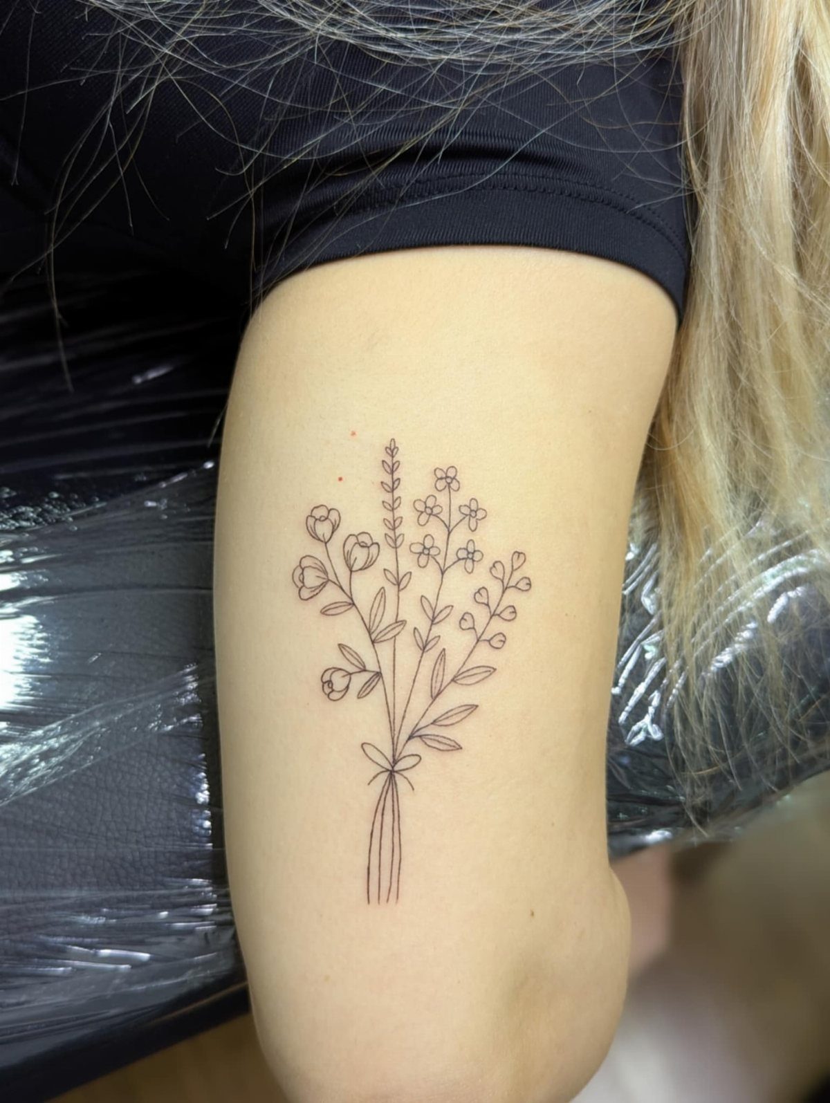 A delicate fine line floral bouquet tattoo on a person's arm.