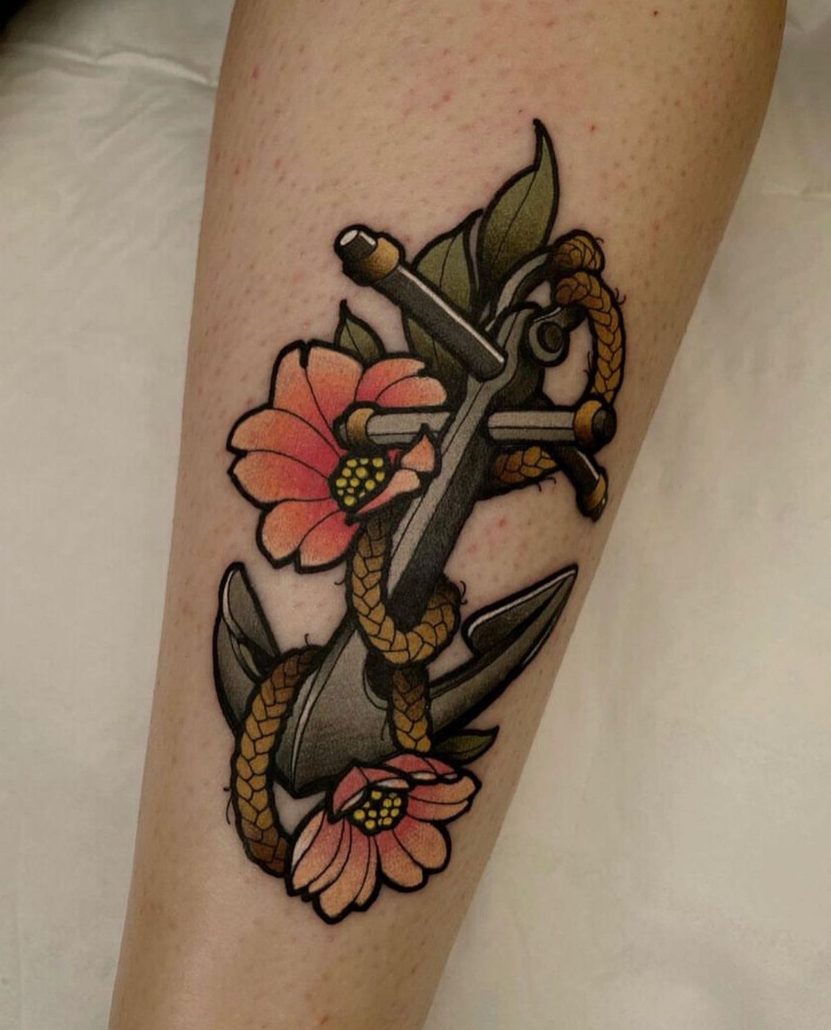 A traditional tattoo of a grey anchor with rope and pink flowers on skin.