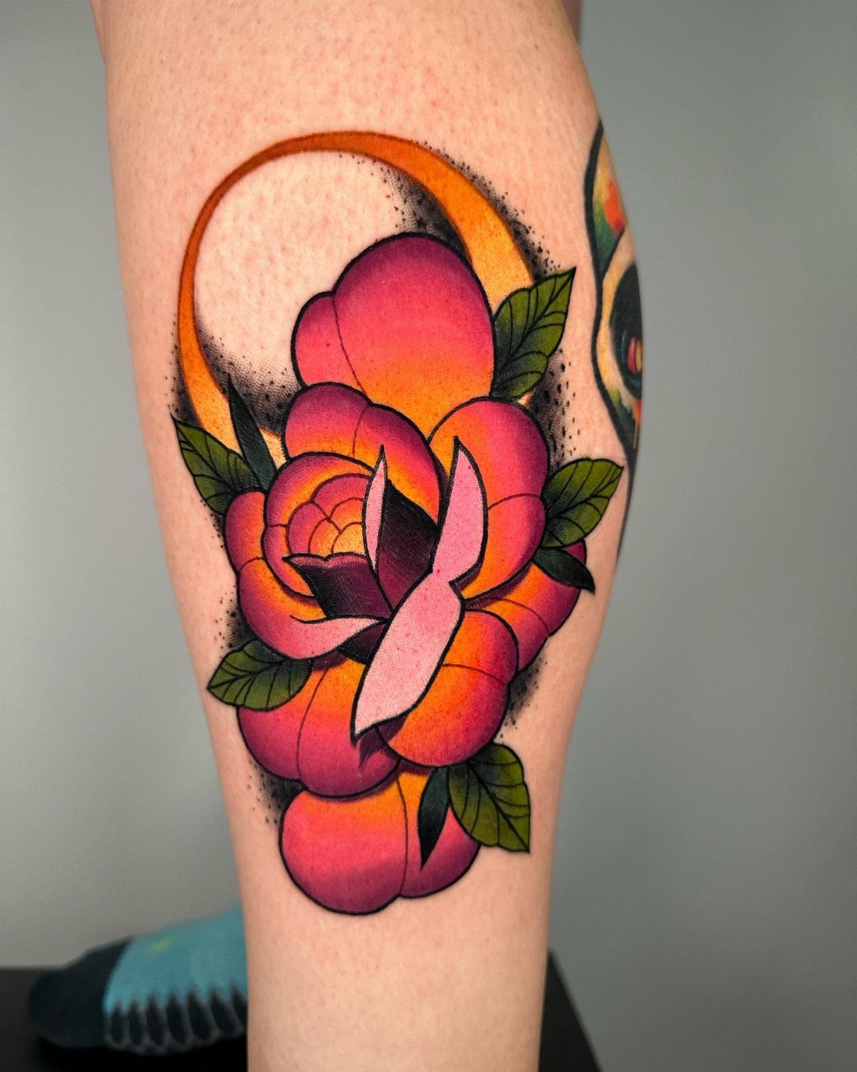 A vibrant traditional rose tattoo with pink petals and green leaves on a person's skin.