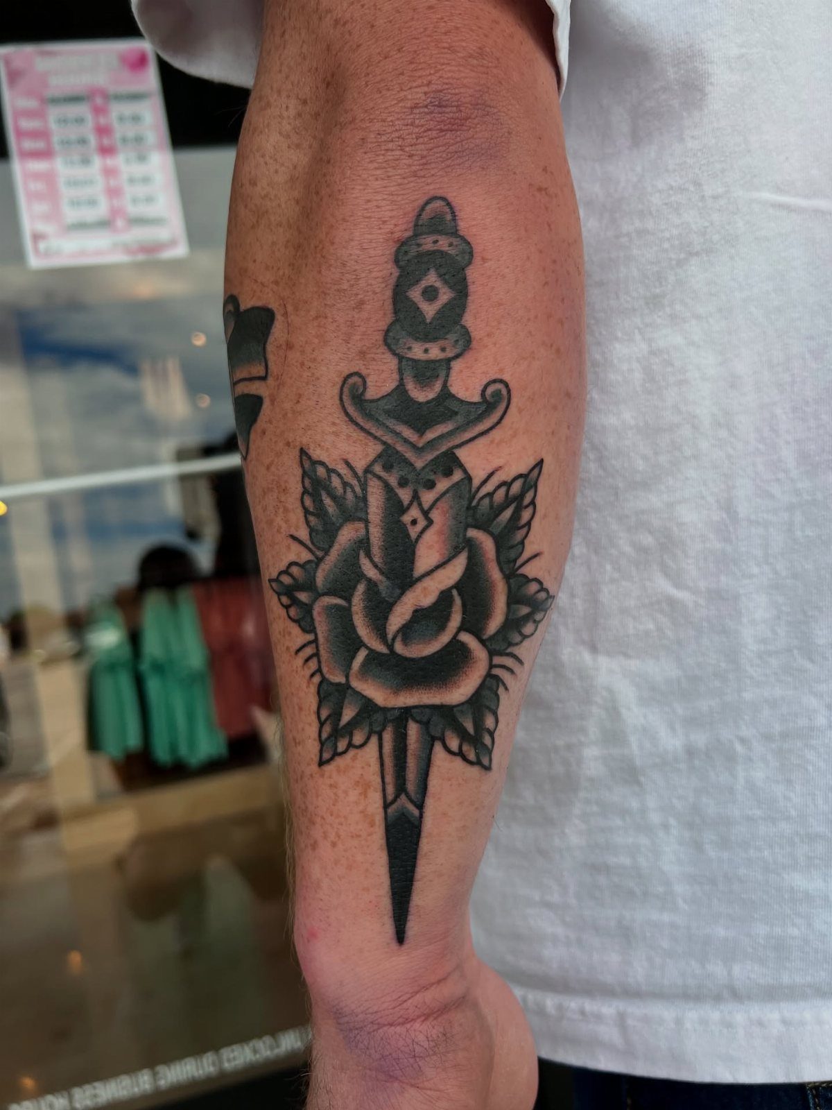 A black ink dagger and rose tattoo on a person's forearm.