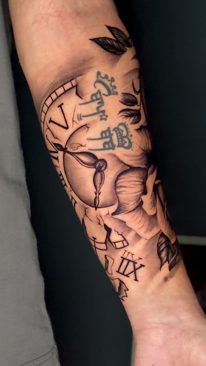A black and grey forearm tattoo depicting a fragmented clock face with Roman numerals and shards.
