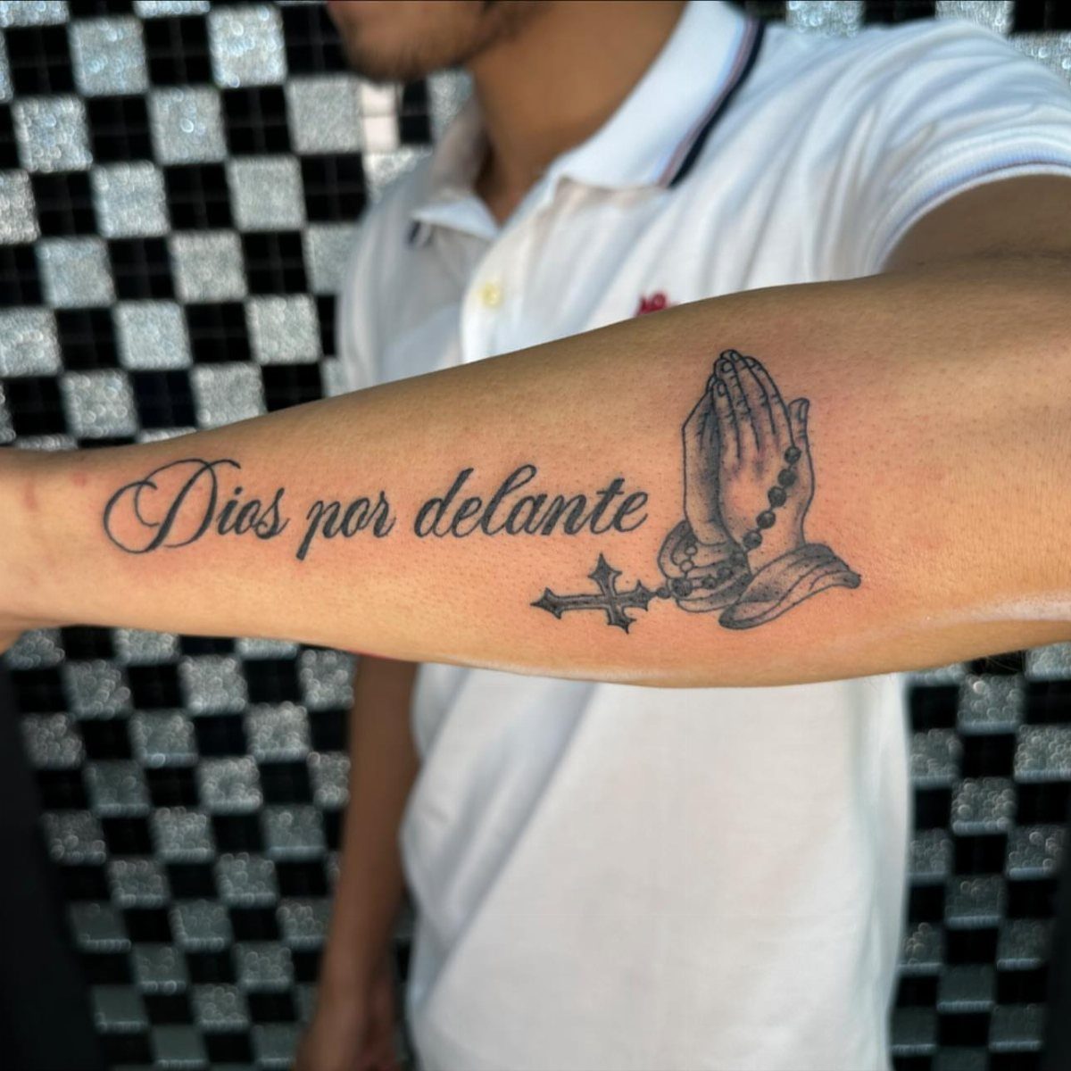 Tattoo on a forearm showing praying hands with a rosary and Spanish text.
