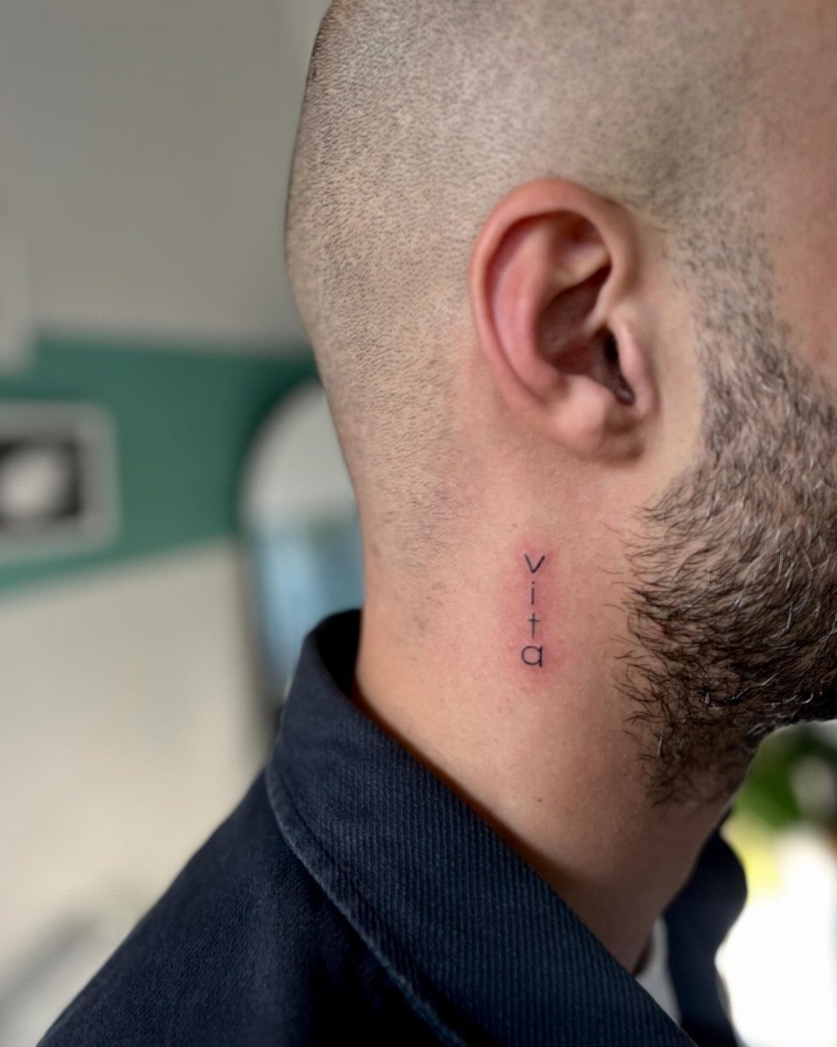 A small minimalist tattoo of the word vita on a man's neck.